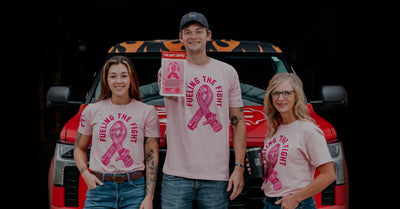 Group of firefighters wearing pink shirts. Man in the middle holding a coffee bag.