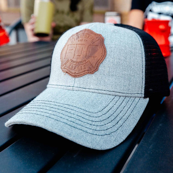 Front/side angle view of grey hat with black mesh back and a leather patch on the front of the FDC maltese cross logo