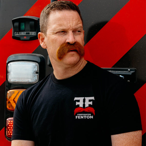 The back of a black shirt with a maltese cross Firefighter Fenton mustache logo. Text around the mustache reads "Salty and I know it, Firefighter Fenton"