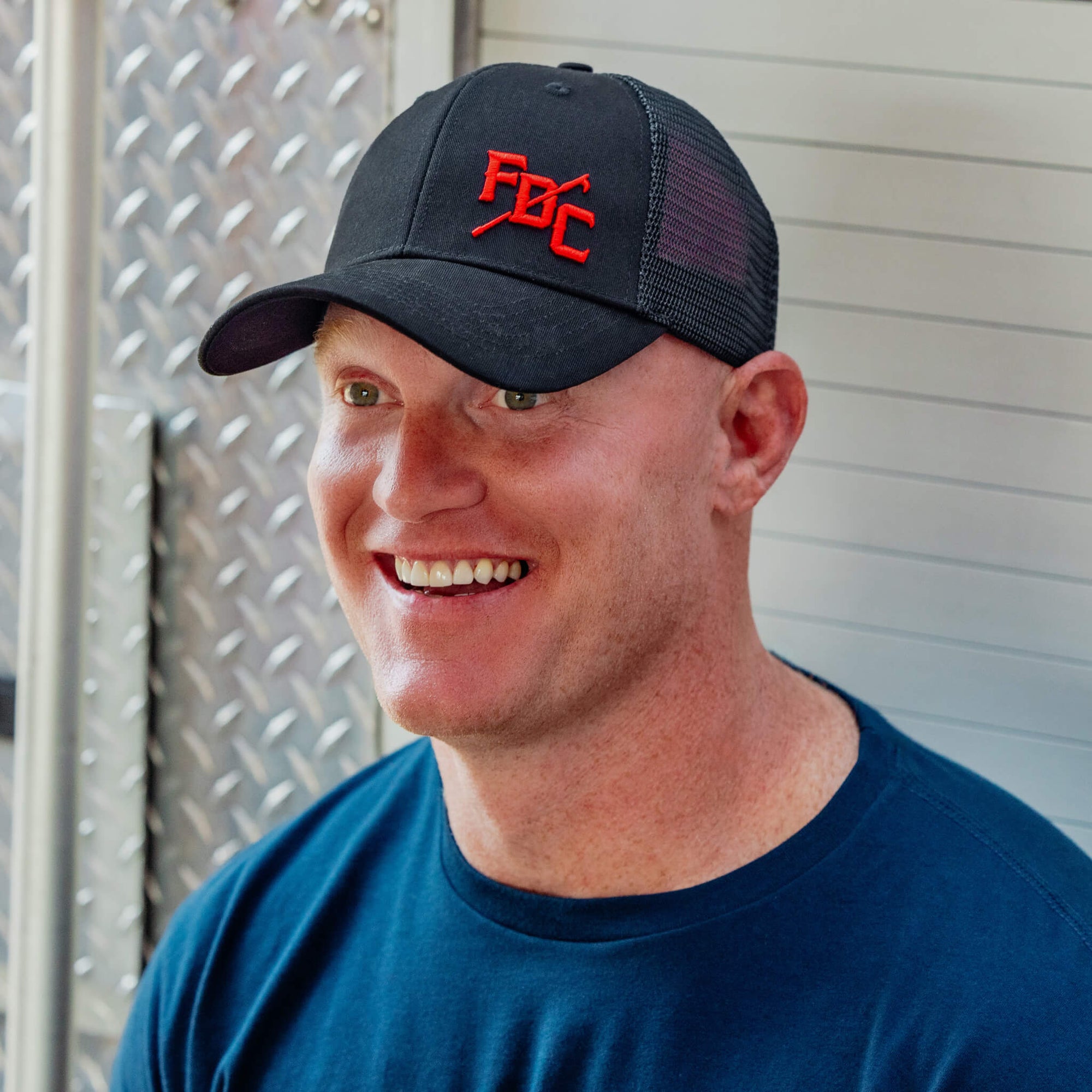 Side view of black hat with mesh back and a red FDC pike pole logo on the front