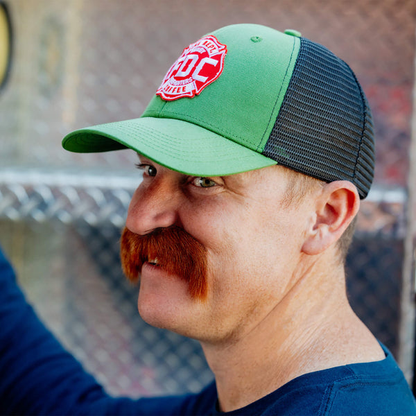 A 3/4 angle image of the FDC Green Hat featuring a green camo design with a red FDC Maltese cross logo on the front.