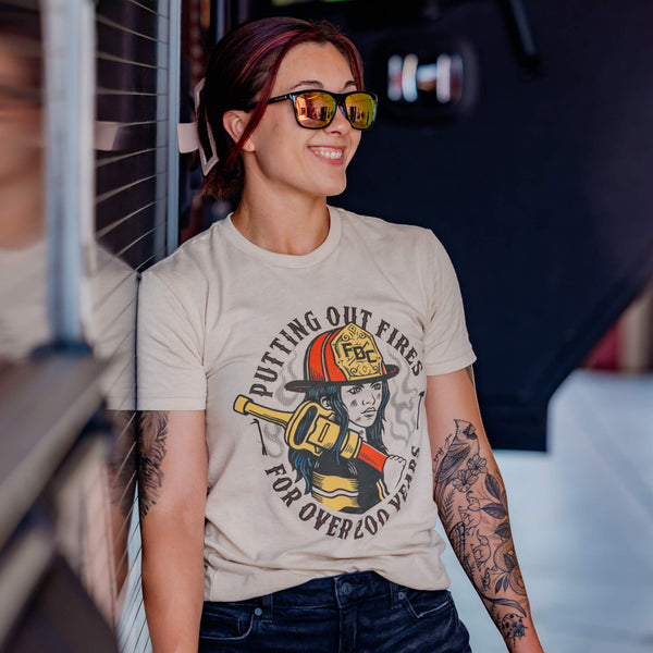 Image of a cream colored shirt with a graphic of a female firefighter on the front of the shirt and text that reads, "Putting out fires for over 200 years"