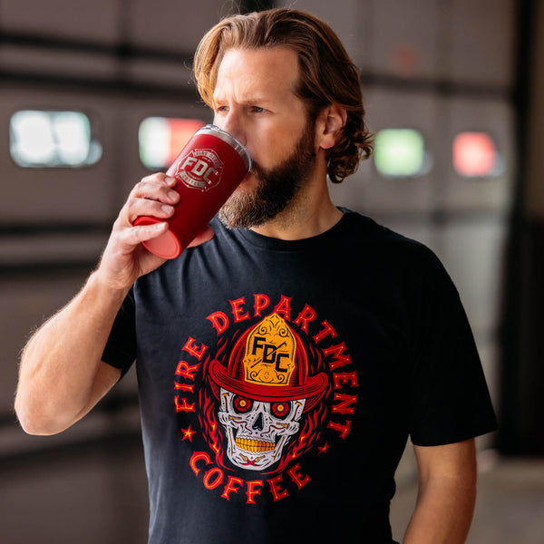 A black t shirt with a skull wearing an FDC fire helmet surrounded by flames in the center. Around the skull is text that reads "Fire Department Coffee".