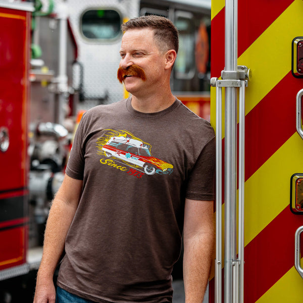 A brown t shirt with a "meat wagon" vehicle on the chest surrounded by flames. Under the vehicle it says "since 1973".