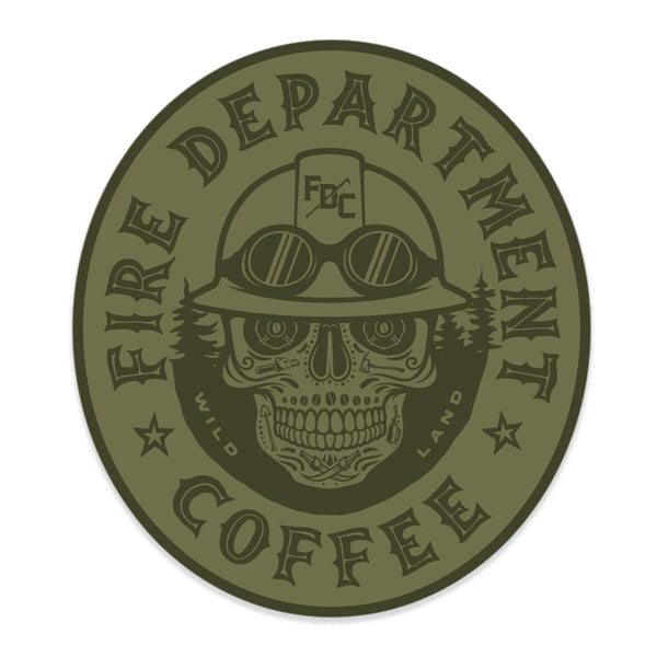 Olive green sticker with "Fire Department Coffee" around the edge of the oval. There is a skull in the middle wearing a firefighting helmet.